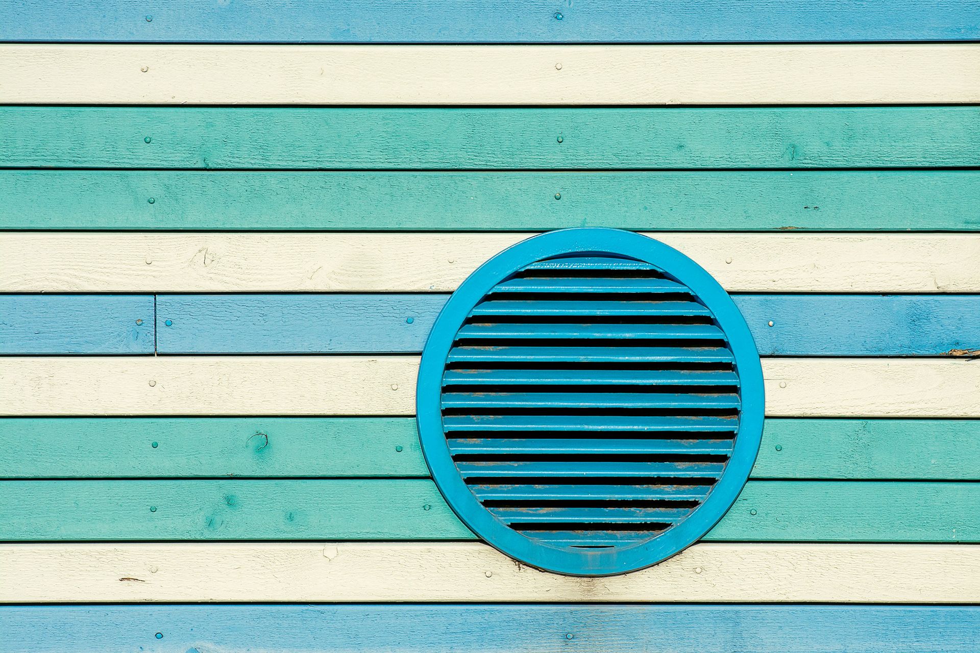 Vibrant blue, green, and cream striped wooden wall with a circular vent.