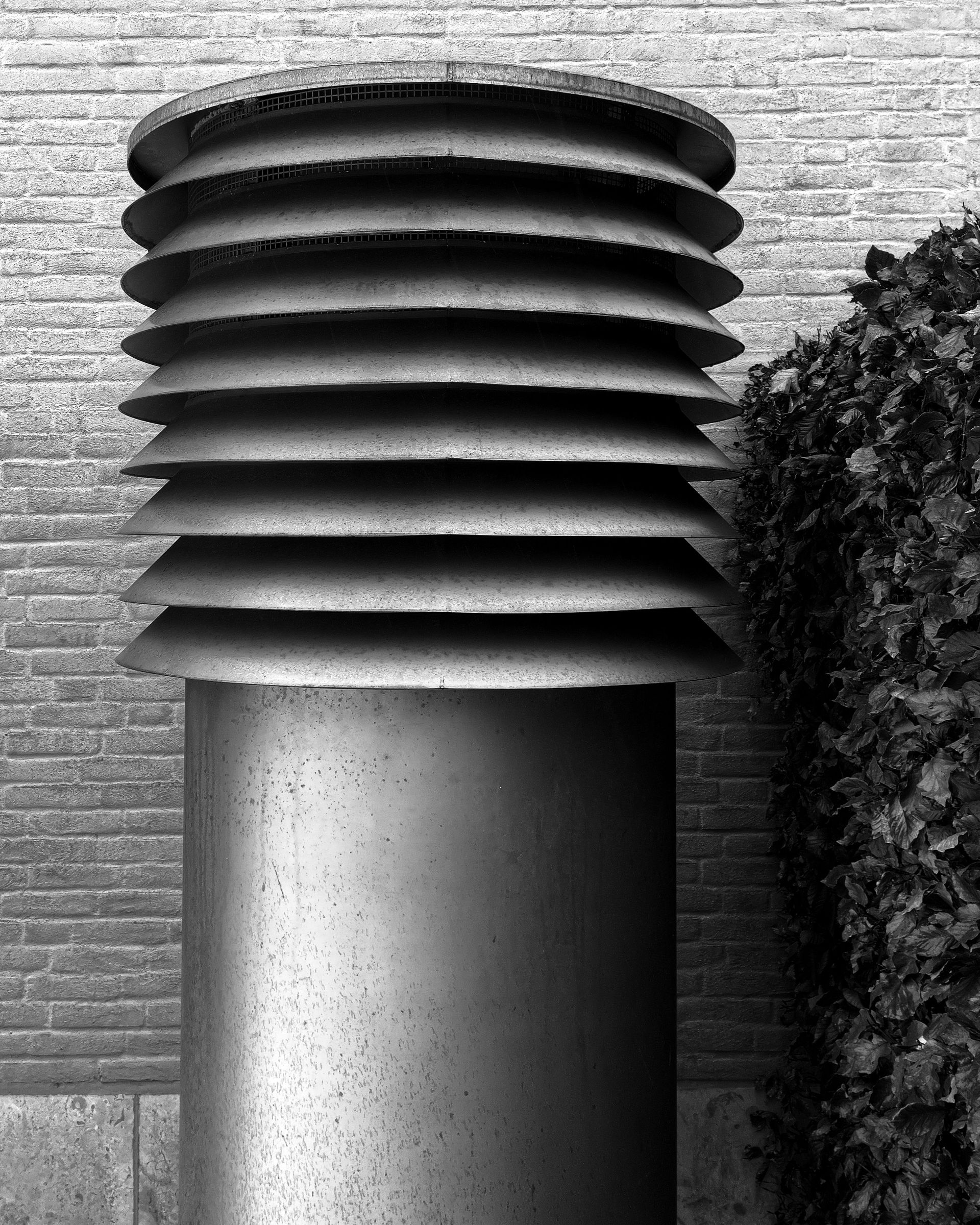 Monochrome image of a large industrial ventilator with geometric design next to a brick wall.