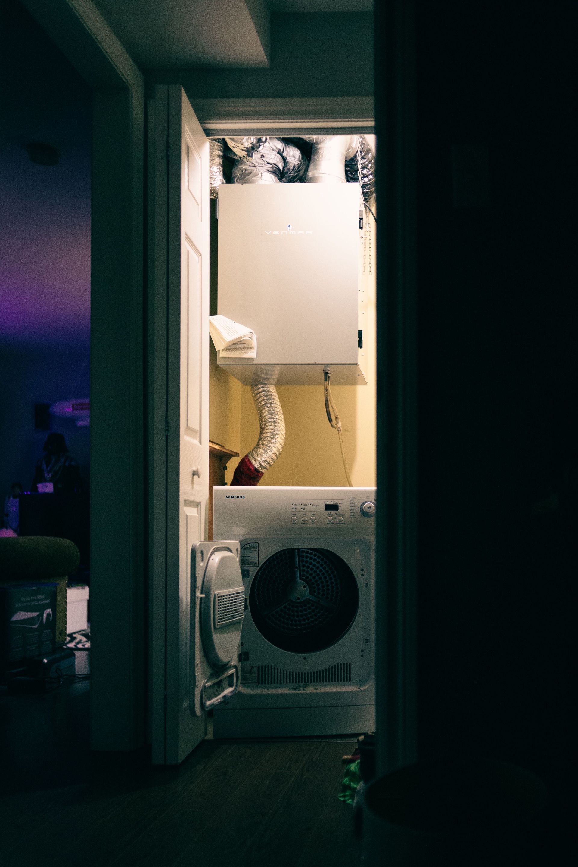 A cozy laundry closet with a dryer and ventilation system, illuminated in low light from indoors.